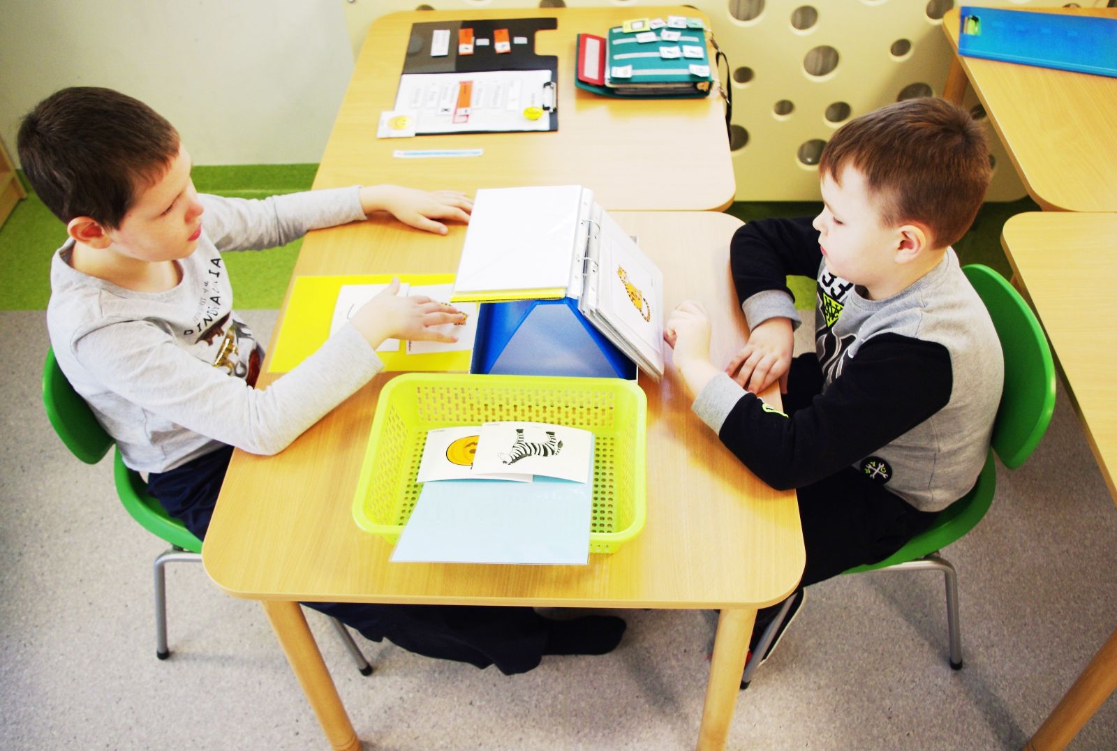 dwoje dzieci siedzi na przeciwko siebie przy stoliku i uczą się języka obrazkowego, czyli alternatywnych metod komunikacji
