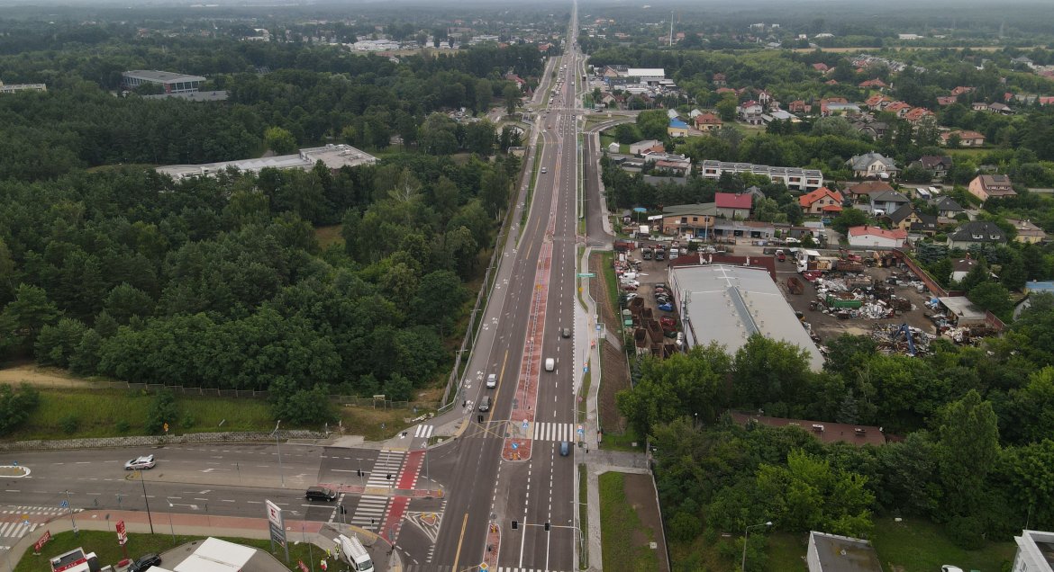 Zdjęcie wykonane z drona. Widok z góry na fragment DK 61 na granicy Legionowa i Michałowa-Reginowa. W centralnym punkcie zdjęcia dwupasmowa droga z infrastruktorą towarzysząca. Po lewej teren Centrum Szkolenia Policji, po prawej domu mieszkalne i budynki usługowe.