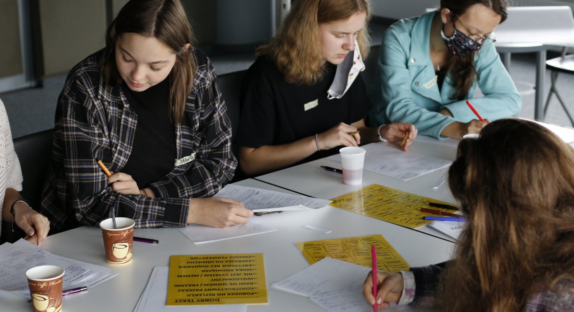 Warsztaty literackie "Kreatywne pisanie z Loesje" poprowadziła Marta Twarowska z fundacji Loesje Polska. Uczestnicy spotkali się 2 października w legionowskiej Miejskiej Bibliotece Publicznej, która była partnerem wydarzenia. Zdjęcie przedstawia kobiety siedzące przy stole.  Zapisują na kartkach słowa.