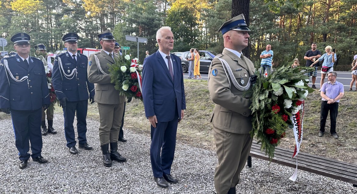 Zdjęcie przedstawia osoby oddające hołd uczestnikom Bitwy Warszawskiej. Po prawej zołnierz z bieńcem z biało czerwona szarfą, za nim rdny powiau Legionowskiego Andrzej Olechowski, dalej stoją przedstawiciele wojska i policji.