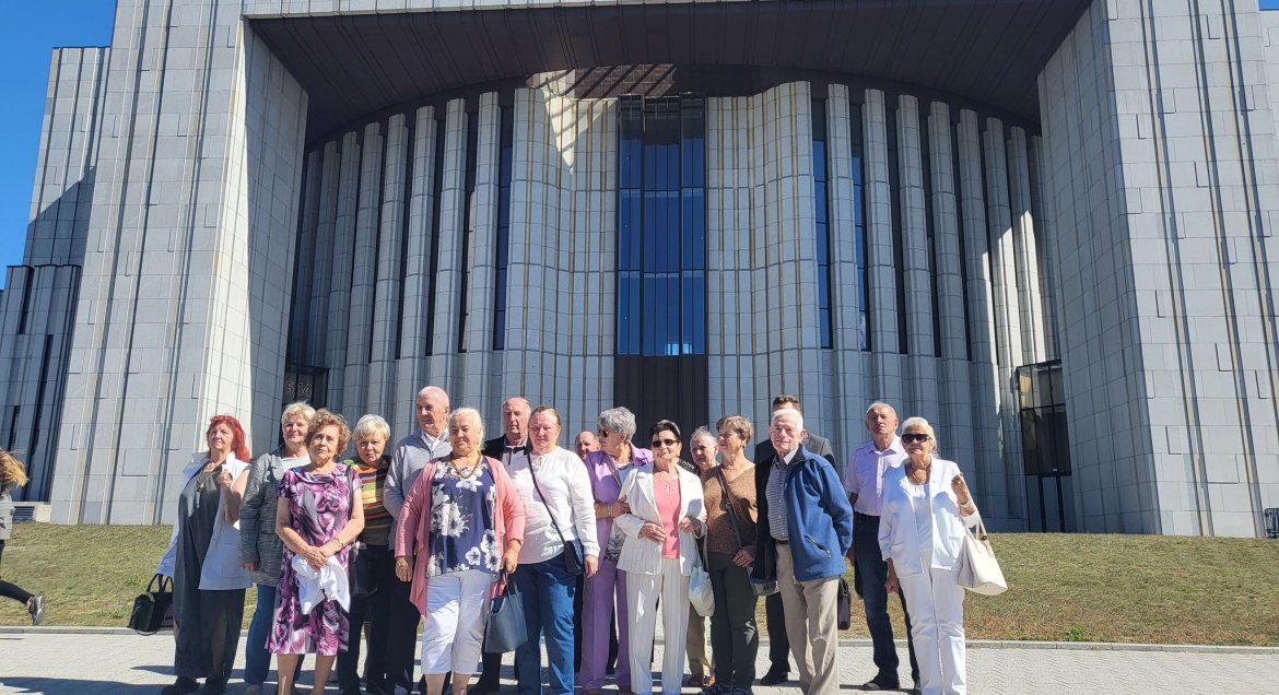 Grupa seniorów stojąca na tle budynku - swiątyni.