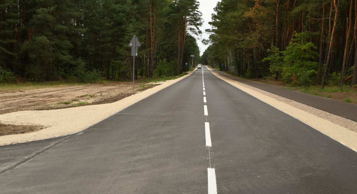 Zdjęcie przedstawia fragment wyremontowanej drogi. Asfalt, pobocze, zieleń otaczająca drogę.