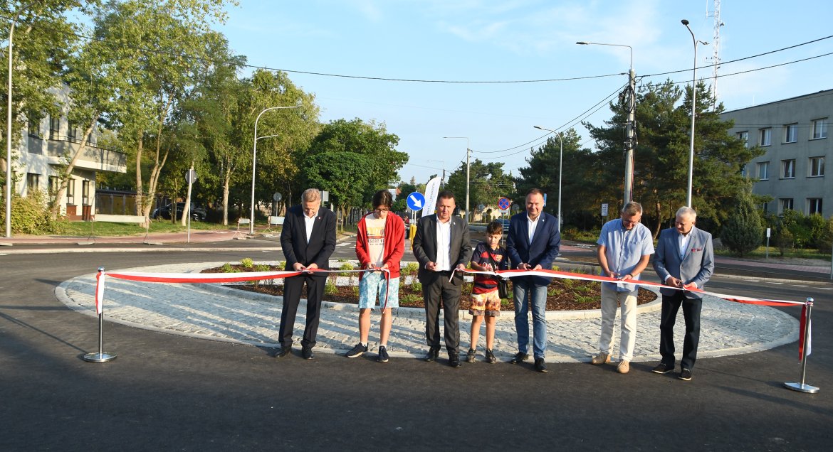 Zdjęcie przedstawia rondo na skrzyzowaniu ulic Jagiellońskiej i Mickiewicza w Legionowie. Szcześć osób dokonuje uroczystego przecięcia wstegi. Wydarzenie - otwarcie ronda 30 sierpnia 2024 r.