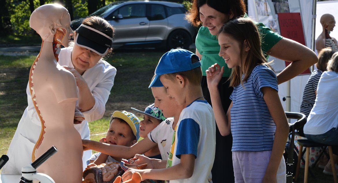 Zdjęcie wykonane w parku przy Pałacu w Jabłonnie. Grua dzieci z opiekunem ogląda eksponaty biologiczne w stoisku Liceum nr 2 w Legionowie.