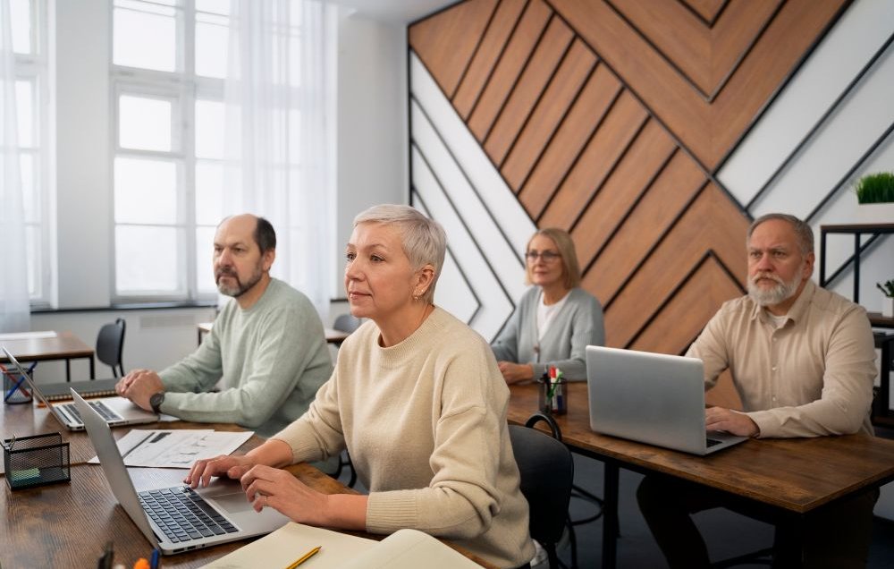 Na zdjęciu seniorzy siedzący w sali wykładowej przed laptopami.