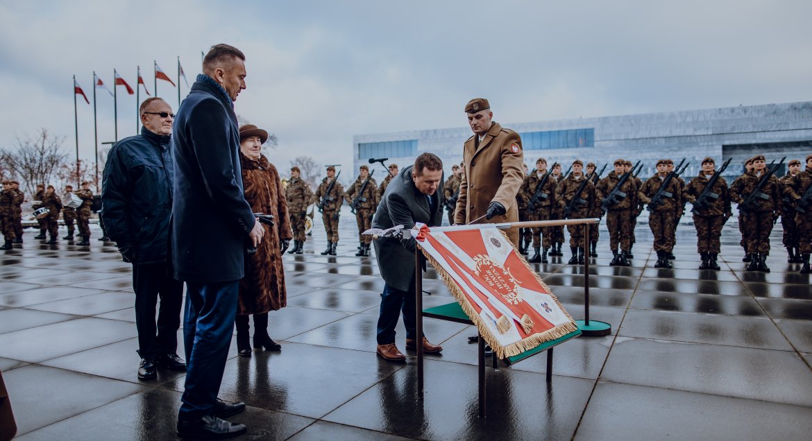 Na zdjęciu starosta przy sztandarze, na placu, w tle żołnierze, flagi polski, fot. DWOT