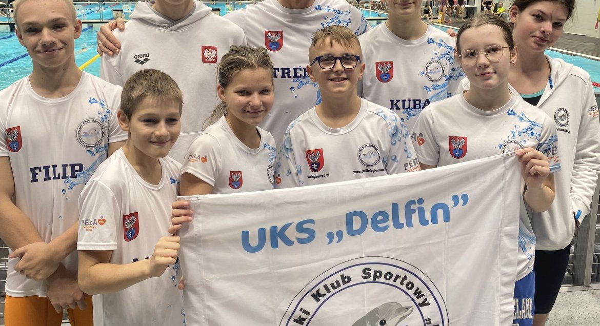 Na zdjęciu jest grupa zawodników z flagą Uczniowskiego Klubu Sportowego Delfin Legionowo