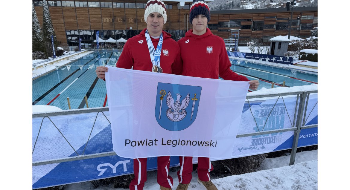 Na zdjęciu zawodnicy Michał oraz Maciej Perl z flagą Powiatu Legionowskiego na tle pływalni.