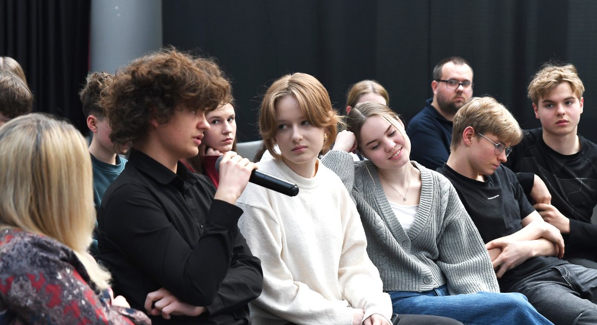 Zdjęcie wykonane w sali konferencyjnej Poczytalnie w Legionowie. Grupa młodzieży dysktuje. Chłopak na pierwszym planie mówi do mikrofonu.