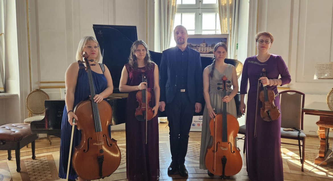 Piecioosobowa grupa muzyków (dwie kobiety, mężczyzna, dwie kobiety) pozuja z instrumentami smyczkowymi w zabutkowej sali balowej Pałacu w Jabłonnie.
