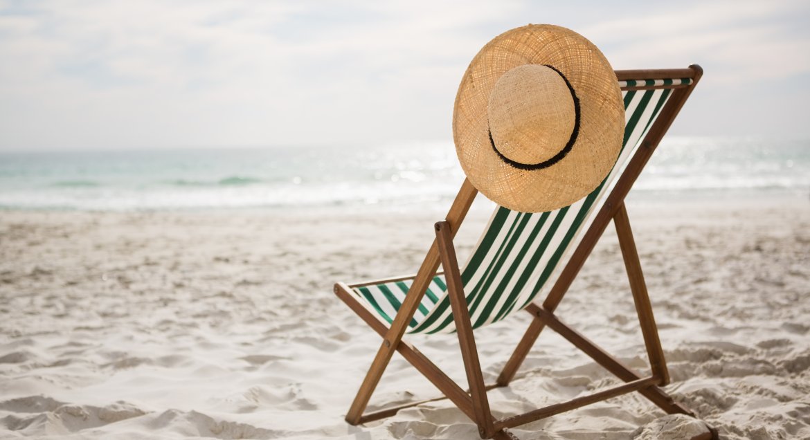 Obraz autorstwa awesomecontent na Freepik. Stojący na plaży leżak w paski, na oparciu wisi słomkowy kapelusz.