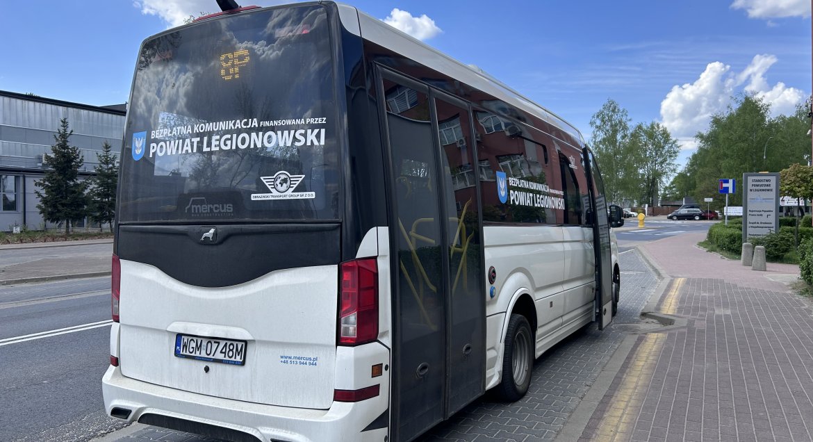 Biały autobus powiatowej komunikacji autobusowej stojący na przystanku, widok z tyłu.