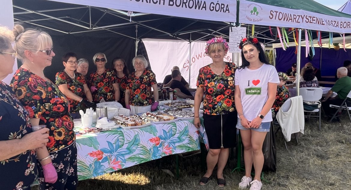 na zdjęciu stoiska, przed nimi kobietu ubrane w kwieciste stroje