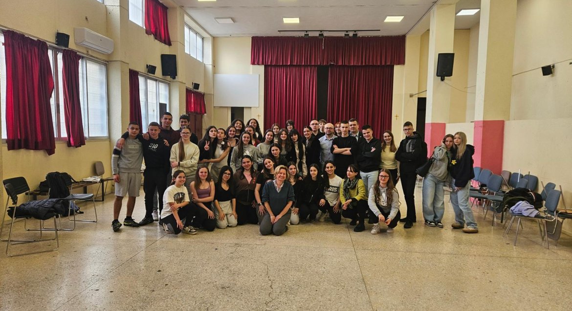 Zdjęcie grupowe przedstawiająca młodzież pozująca na sali na tle kurtyny.