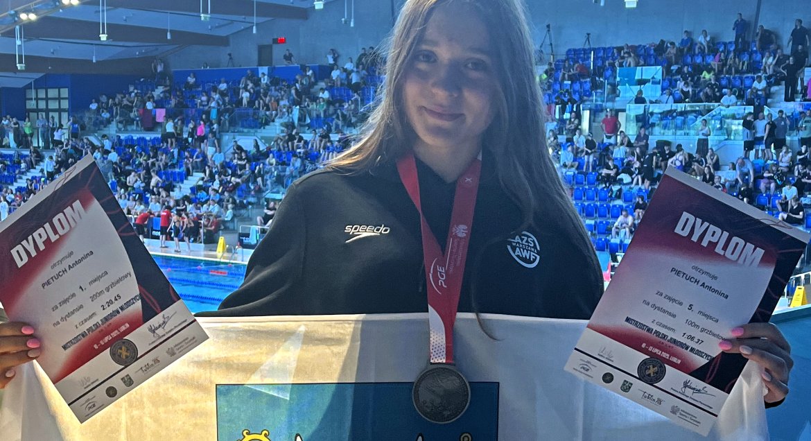 Na zdjęciu Antonina Pietuch z flagą Powiatu, medalem i dyplomami na tle pływalni