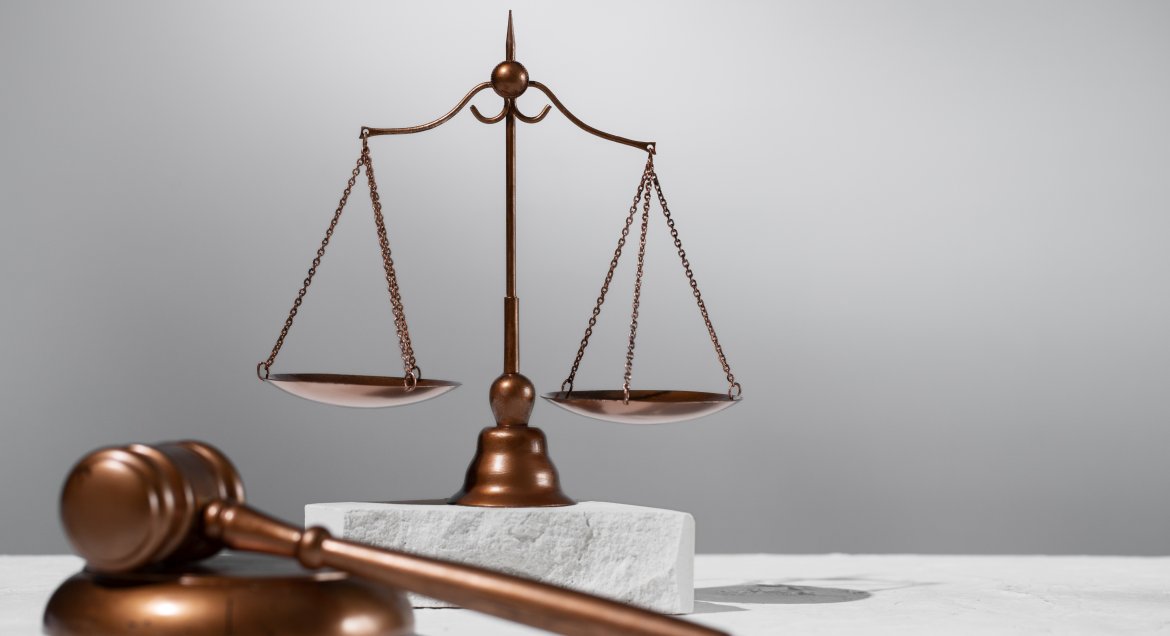 Zdjęcie - waga szalkowa symbol sprawiedliwości oraz atrubuty sędziowskie drewniany młotek i podkładka.