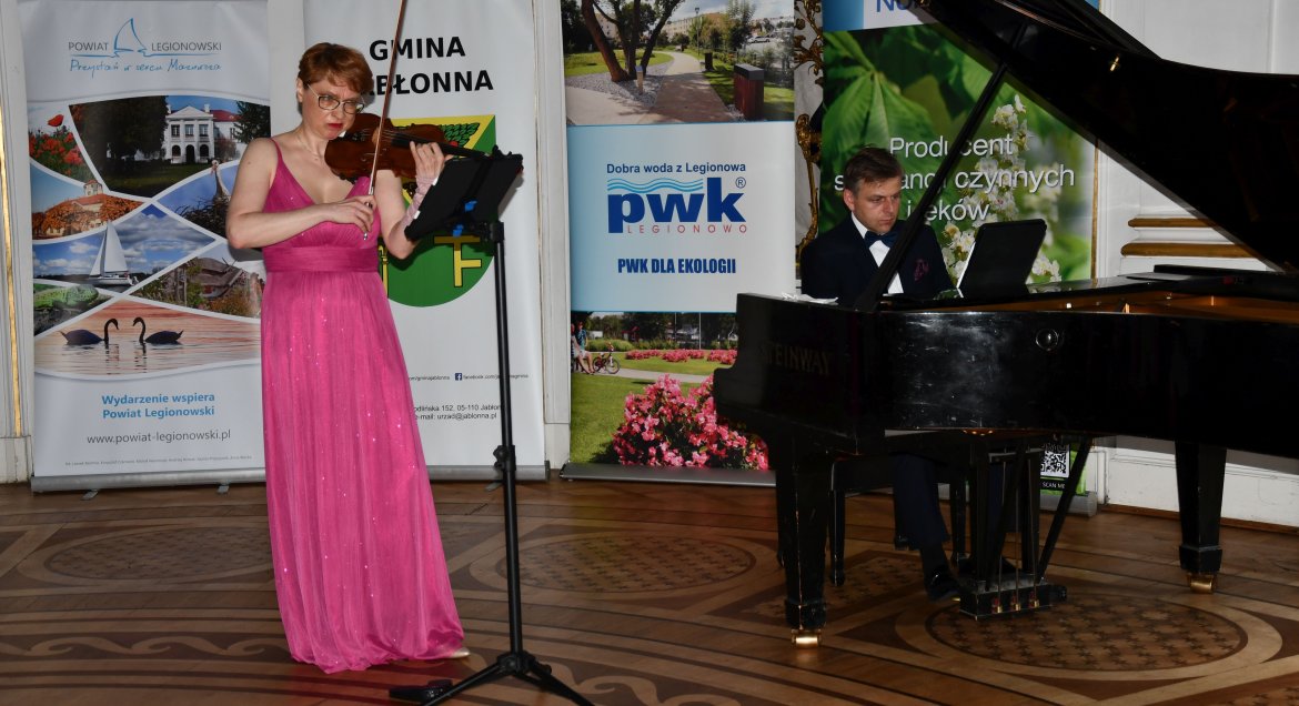 Na zdjęciu widać ubraną w różową suknię skrzypaczkę i pianistę siedzącego za fotrepianem