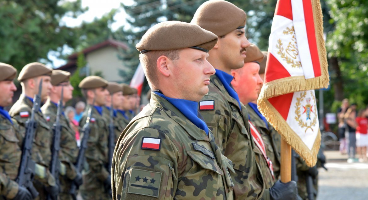 Zdjęcie przedstawia żołnierzy Wojska Polskiego stojacych w dwuszeregu. Na pierwszym planie dwóch mężczyzn ze sztandarem.