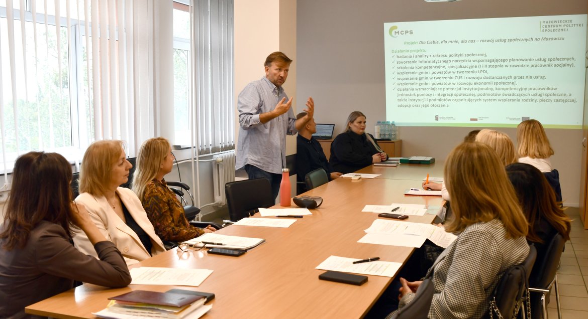 Szkolenie, uczestnicy przy stole, siedzą na krzesław, obok wykładowca