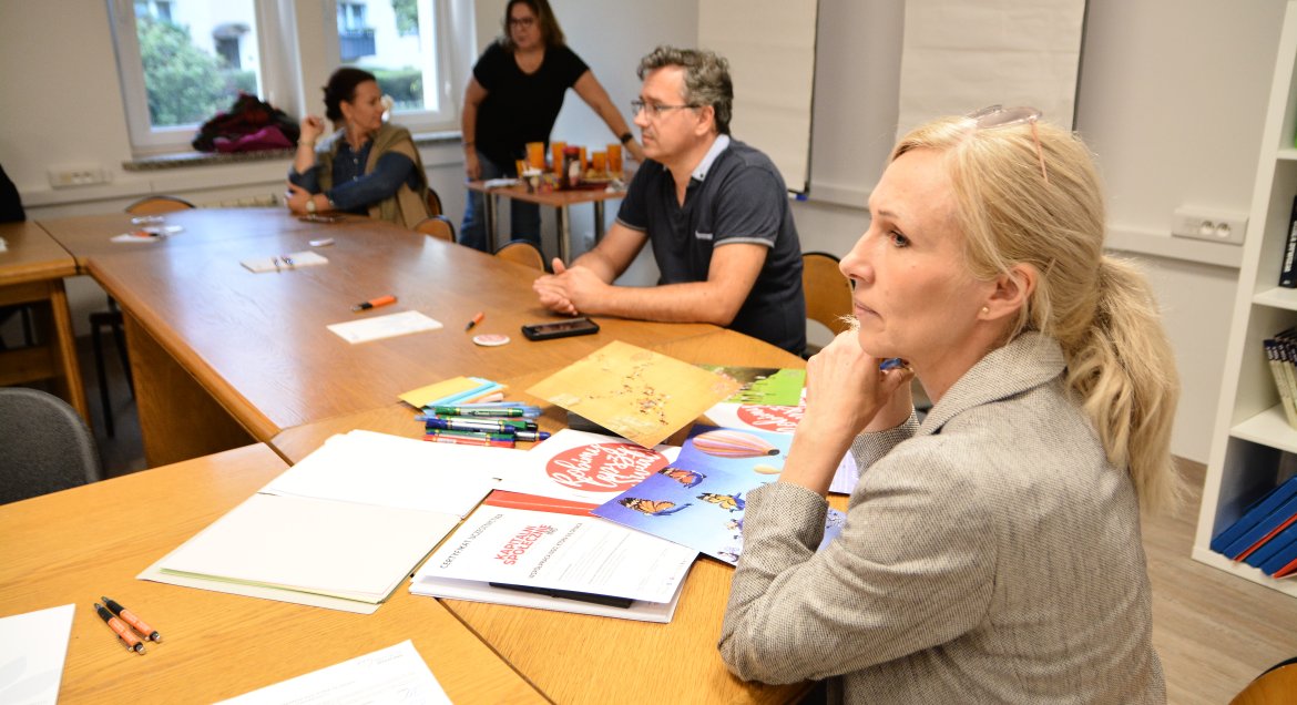 Zdjęcie: grupa osób pracuje przy stolikach, na których leżą materiały.