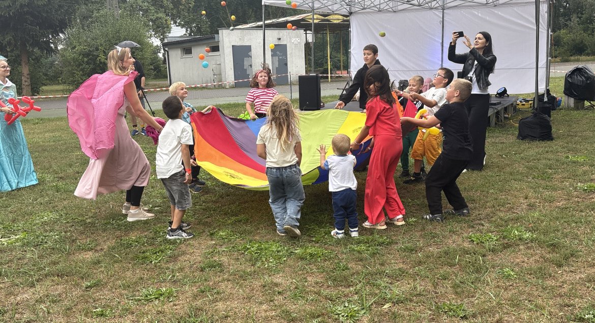 Zdjęcie wykonane w Kompleksie Rekreacyjno-Wypoczynkowym Nieporęt-Pilawa, grupa dzieci uczetniczy w zabawie z kolorowa chustą.