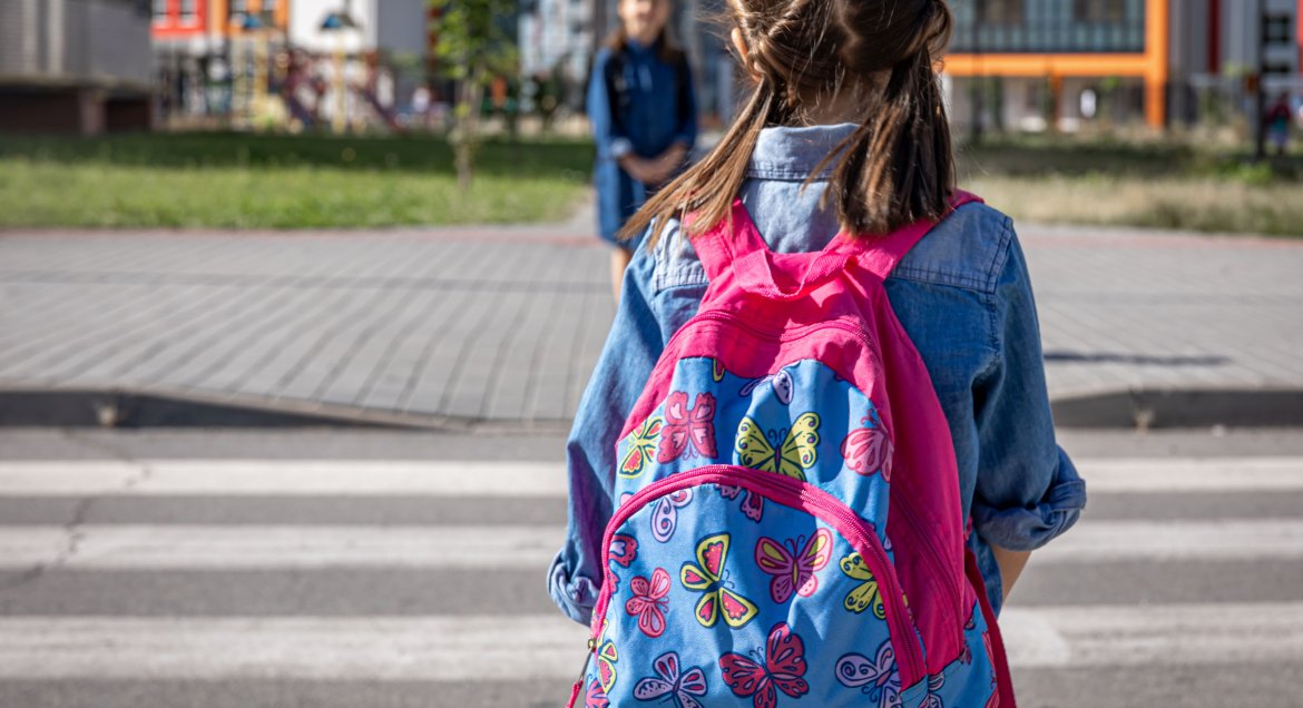 Na zdjęciu dziewczynka stojąca tyłem ze szkolnym plecakiem na plecach