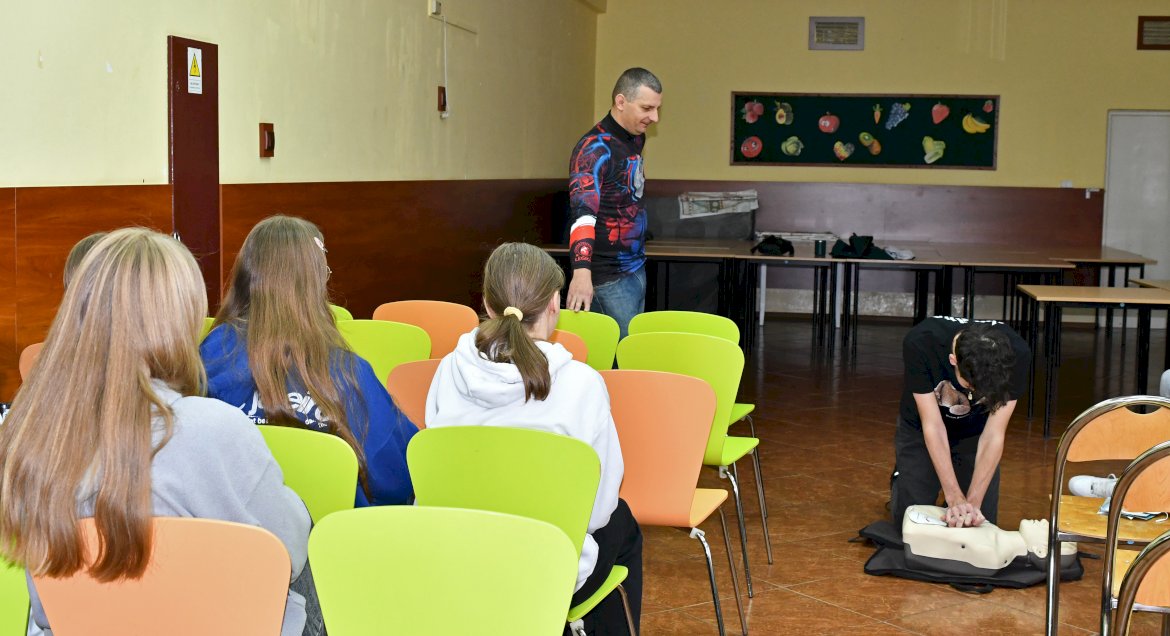 Na zdjęciu osoba ucząca się RKO na fantomie, z boku siedzą inni uczestnicy szkolenia