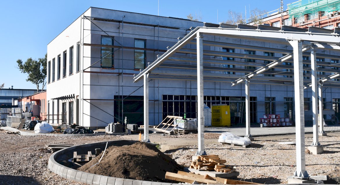 Zdjecie z placu budowy, na pierwszym planie wiata fotowoltaiczna nad miejscami parkingowymi, w tle nowy budynek Starostwa.