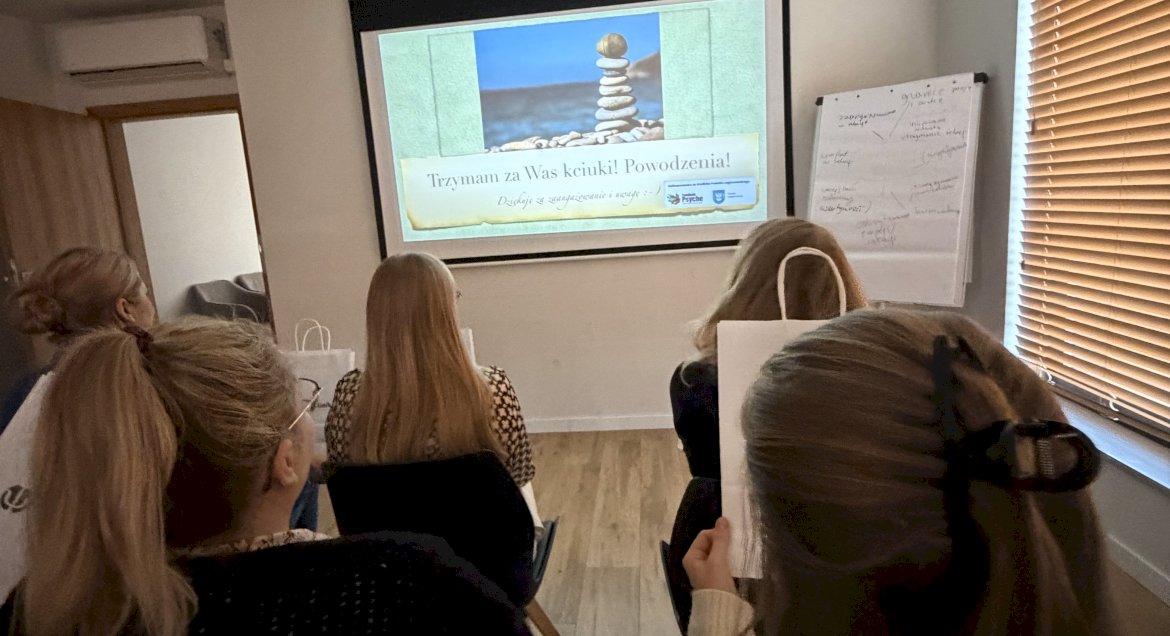 Osoby siedzące tyłem w sali wykładowej, w tle ekran z prezentacją.