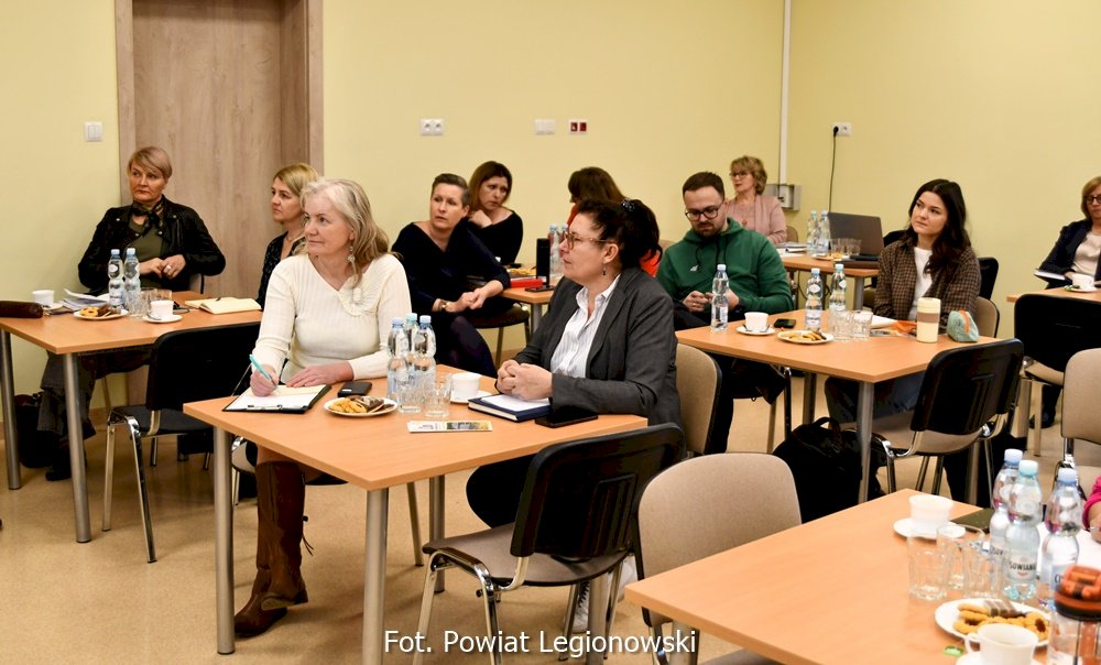 Grupa odób siedząca przy stolikach i słuchająca wykładu podczas spotkania w Poradni Psychologiczno-Pedagogicznej w Legionowie.