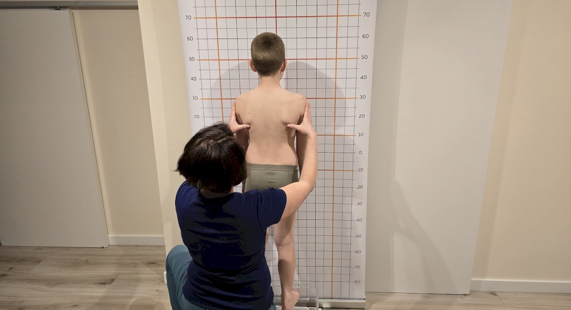 Na zdjęciu fizjoterapeuta wykonuje badanie kręgosłupa chłopca