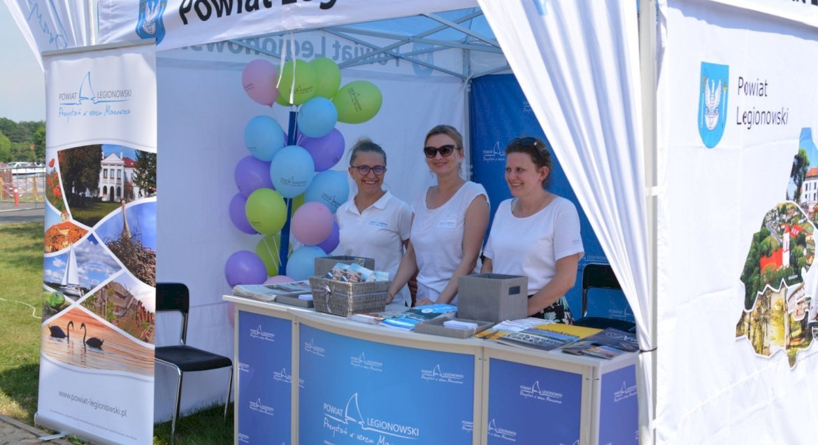 Zdjęcie stoika promocyjnego Powiatu Legionowskiego, ww rodku trzy osoby przy ladzie