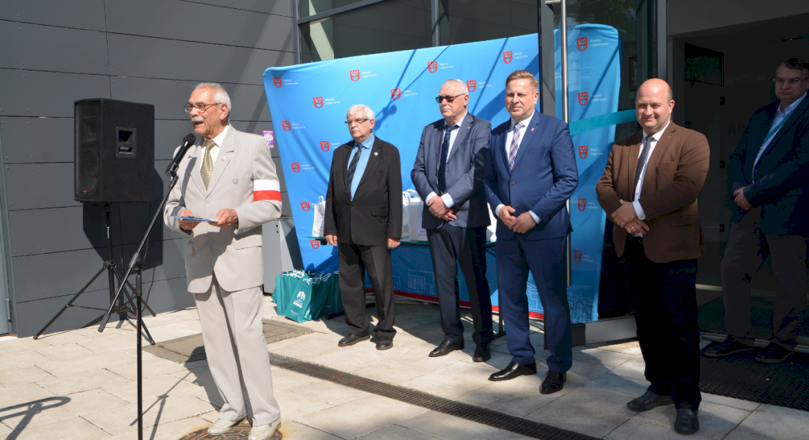 Na zdjęciu widać grupę mężczyzn przedstawicieli różnych środowisk, w tym jeden z nich przemawia przez mikrofon