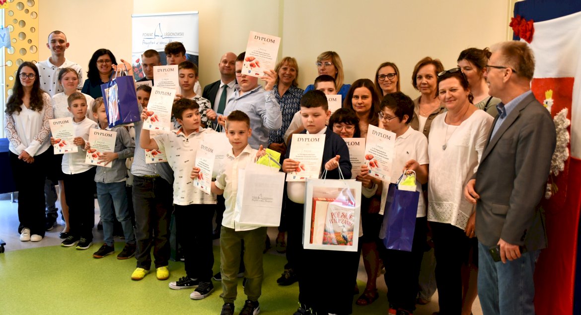 Na zdjęciu grupa uczniów szkół specjalnych ubranych wgalowe stroje z dyplomami w rękach i pośród nich dorośli organizatorzy
