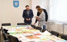 Komisja konkursowa nad pracami, na stole leży dużo rysunków, stoją trzy osoby