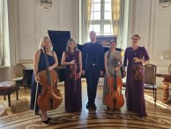 Piecioosobowa grupa muzyków (dwie kobiety, mężczyzna, dwie kobiety) pozuja z instrumentami smyczkowymi w zabutkowej sali balowej Pałacu w Jabłonnie.