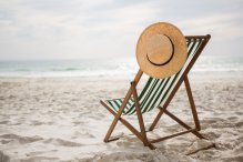 Obraz autorstwa awesomecontent na Freepik. Stojący na plaży leżak w paski, na oparciu wisi słomkowy kapelusz.