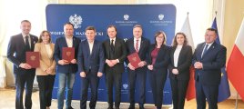 Grupa przedstawicieli władz samorządowych z terenu Mazowsze podczas pamiątkowego zdjęcia, pozują na granatowej ściance promocyjnej Wojewody Mazowieckiego.