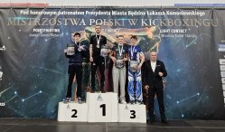 Zawodnicy na podium, z medalami i dyplomamy, z tyłu baner z napisem Mistrzostwa Polski w Kickboxingu