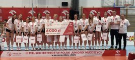 na zdjęciu drużyna siatkarek na podium, koło nich czek na 6 000 zł, na szyi medale, w rękach torby