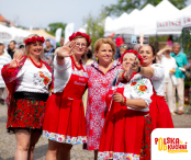 Na zdjęciu widać grupę uśmiechniętych kobiet w tradycyjnych strojach ludowych, pozujących do wspólnego selfie podczas plenerowego wydarzenia kulinarnego. Panie mają czerwone spódnice, kwieciste bluzki i ozdobne wianki na głowach, a w tle widoczne są białe namioty festiwalowe oraz zgromadzeni uczestnicy. W prawym dolnym rogu widnieje logo „Polska Od Kuchni – Festiwal Kulinarny”.