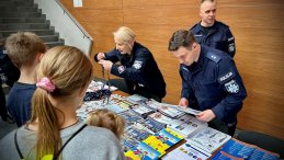 Stoisko CSP, policjanci przed stolikiem z materiałam informacyjnymy, przy stoliku stoją dzieci
