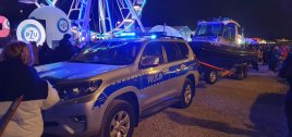 Zdjęcie wozu policyjnego, wieczorem, na przyczepce stoi łódka policyjna, w tle koło diabelski młyn