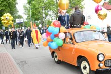 Zdjęcie przedstawia pochów podczas Wojciechowego świętowania. Po lewej idący w pochodzie uczestnicy, po prawej udekorowana balonami, pomaranczowa synekna pickup z orkiestą dęta na pace.
