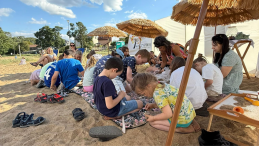 Zdjęcie przedstawia grupę dzieci uczestniczącą w warsztatach ceramicznych na plaży