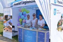 Zdjęcie stoika promocyjnego Powiatu Legionowskiego, ww rodku trzy osoby przy ladzie