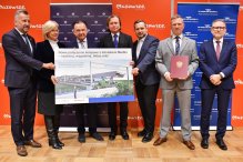 Na zdjęciu grupa osób prezentująca tablicę promująca inwestycję