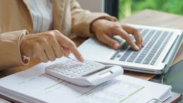 Na zdjęciu widać ręce kobiety, która liczy coś na kalkulatorze i ma przed sobą otwarty laptop