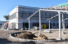 Zdjecie z placu budowy, na pierwszym planie wiata fotowoltaiczna nad miejscami parkingowymi, w tle nowy budynek Starostwa.