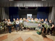 Zdjęcie przedstawia grupę osób ze stroikami w dłoniach, uczestników warsztatów stroikowych w tle rollup Powiatu Legionowskiego